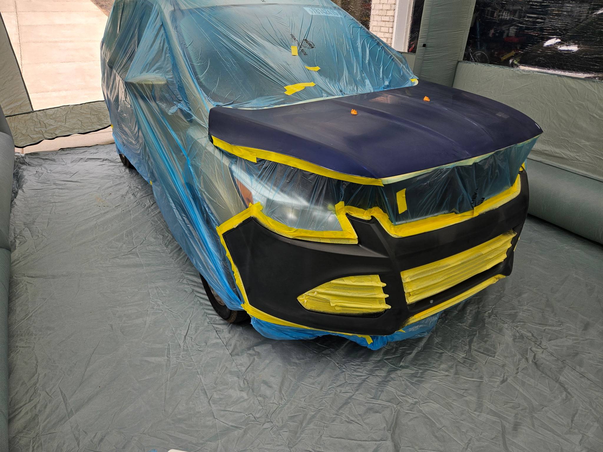 Before photo of 2014 Ford Escape masked off in an inflatable spray booth with hood prepped in primer for repaint