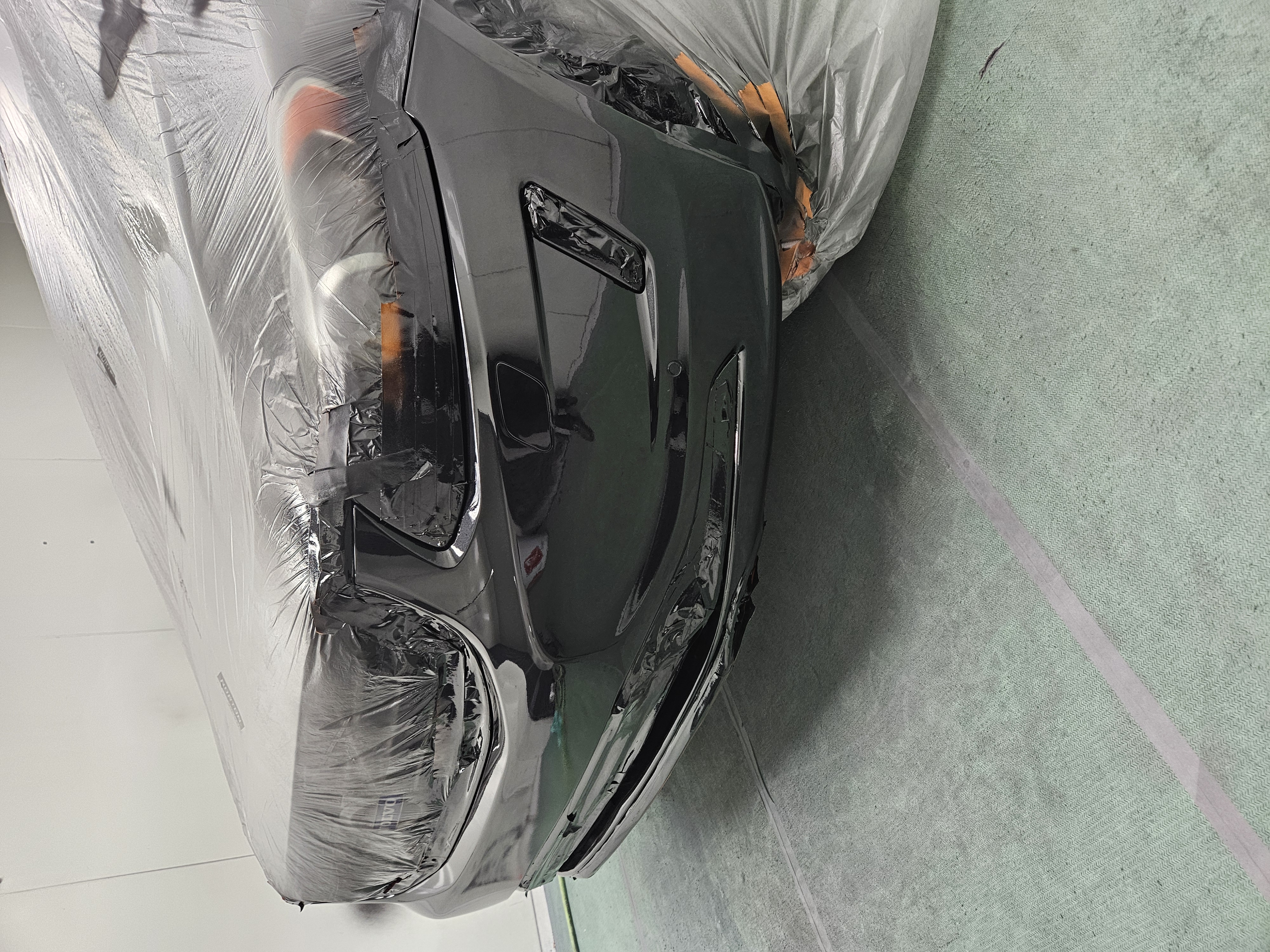 After photo of black SUV front bumper masked in spray booth with fresh refinish and clear coat