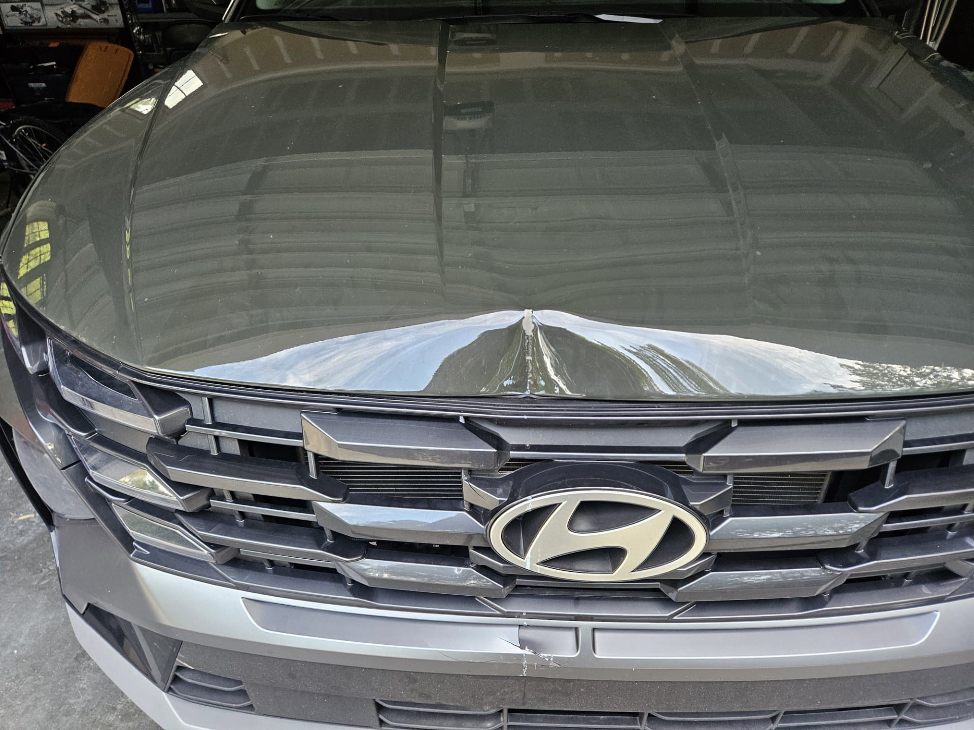 Before photo of gray Hyundai Tucson hood with a sharp impact dent and crease on the front edge above the grille