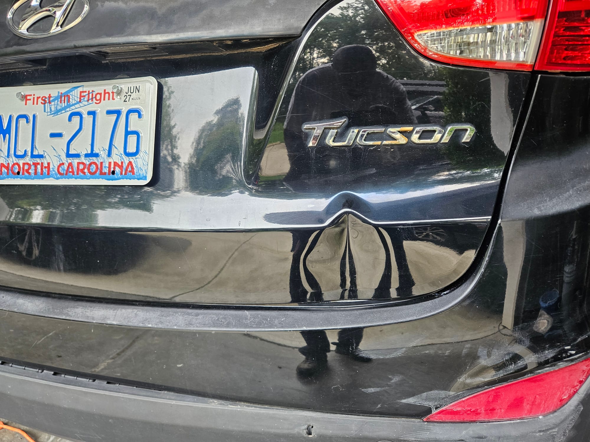 Before photo of black Hyundai Tucson tailgate with an impact dent above the rear bumper seam